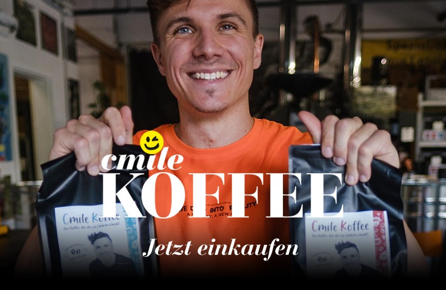 Chris lacht und hält 2 Packungen Kaffee in die Kamera. Auf dem Bild ist die Schrift: cmile Koffee - Jetzt einkaufen zu sehen